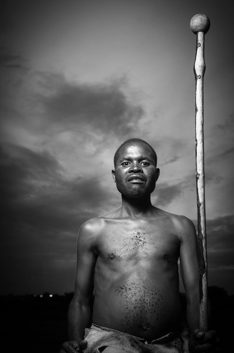 Ngoni man holding a staff against a dramatic sky