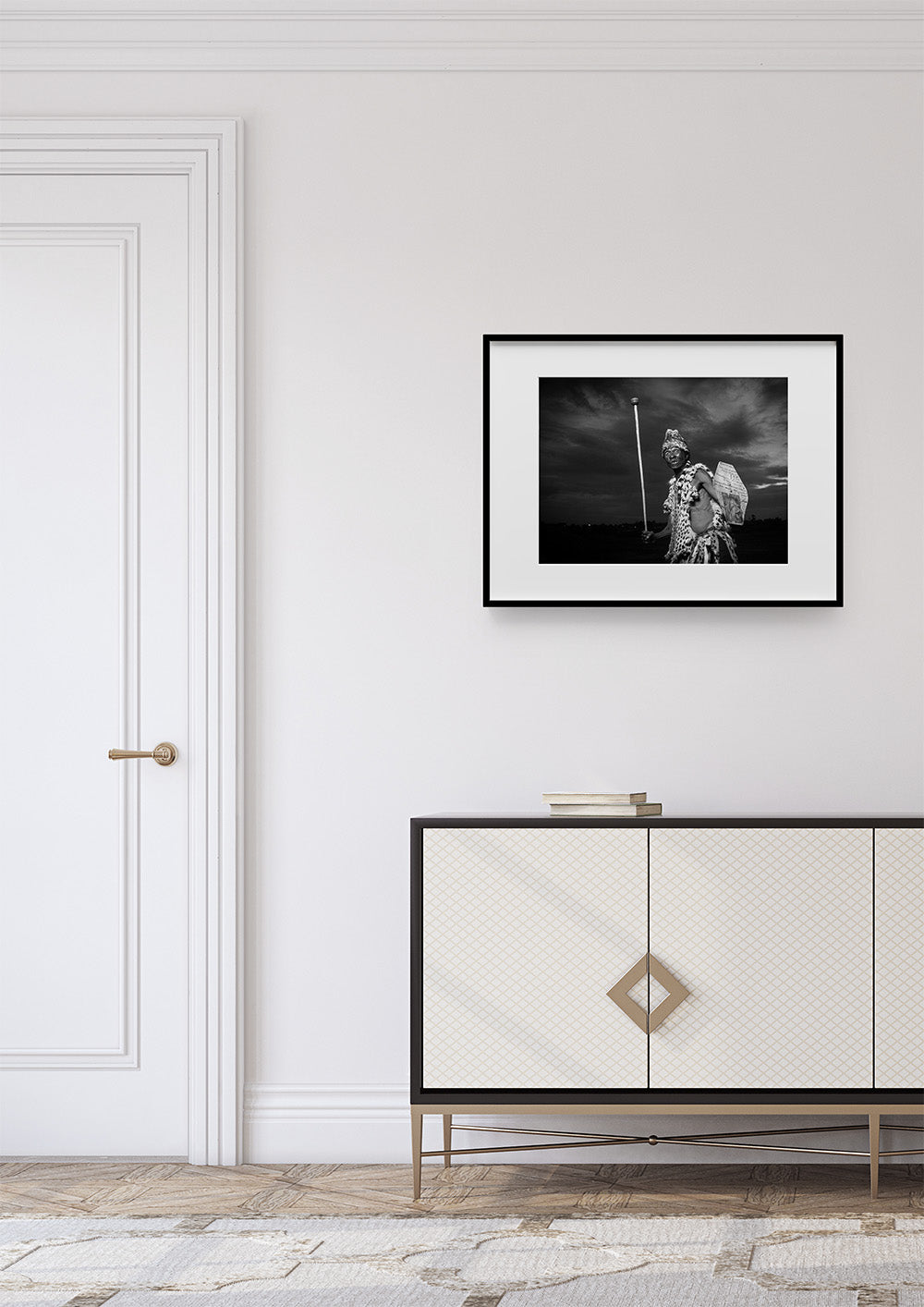 Framed black and white photograph above a white cabinet with gold accents in a room with a white door.